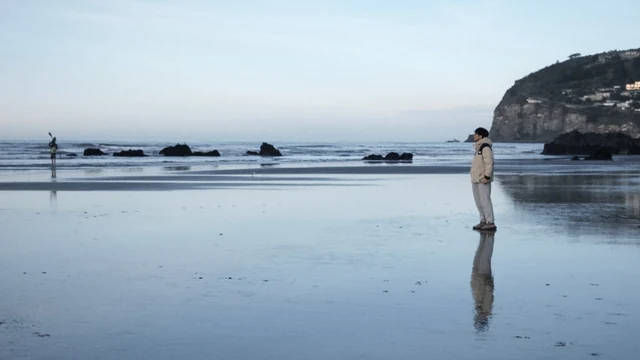 蓝色海湾里的礁石、岸边人物与水面倒影